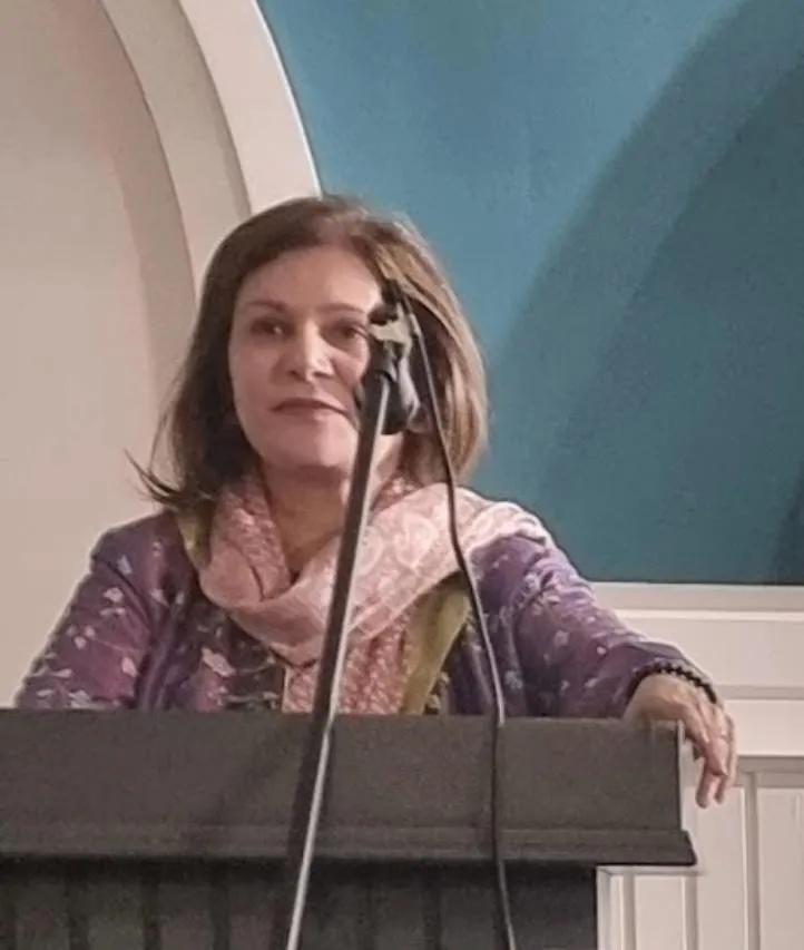 Shefali Chopra speaking at a wooden lectern in warm light